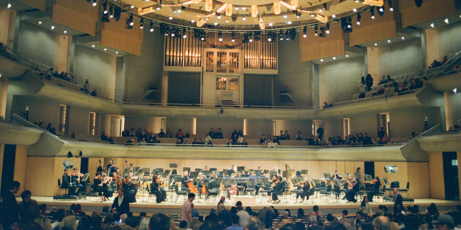 An orchestra on stage in a grand concert hall, with the audience seated around it.